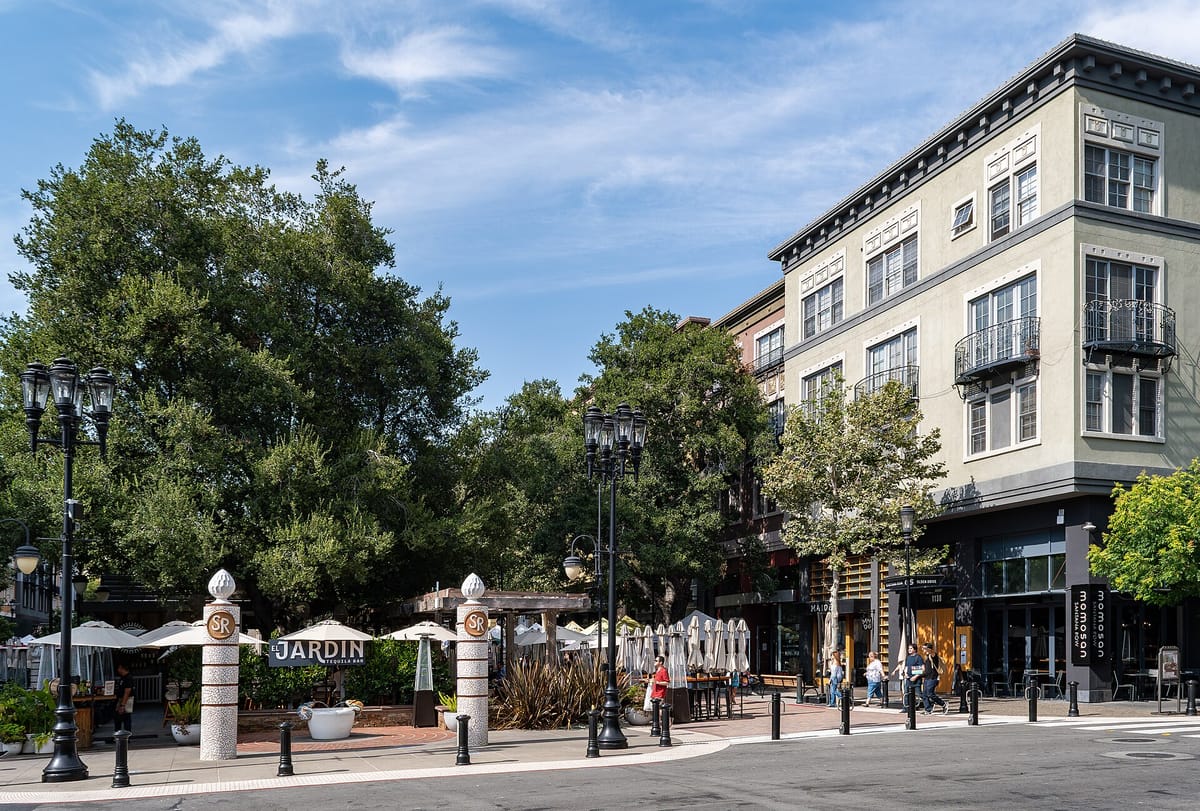 The southern entrance to Santana Row at Olsen Drive, with trees and cafe tables