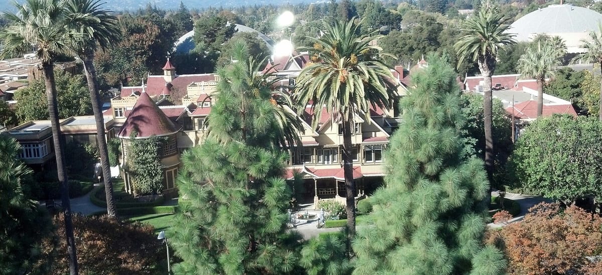 The Winchester Mystery House among palms and pines, seen from a nearby high rise