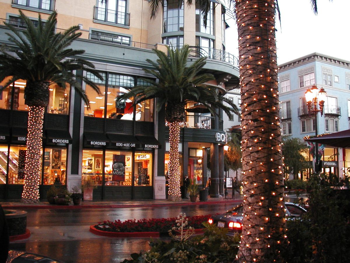Palm trunks wrapped in lights in front of shops on Santana Row on a rainy evening